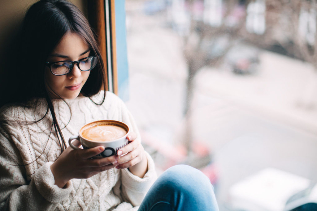 Teenage girl sitting at a window and holding a cup of coffee on a cold autumn day