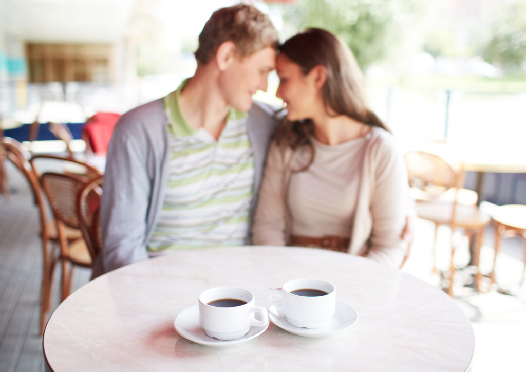 Image of two cups of coffee on table with romantic couple on background